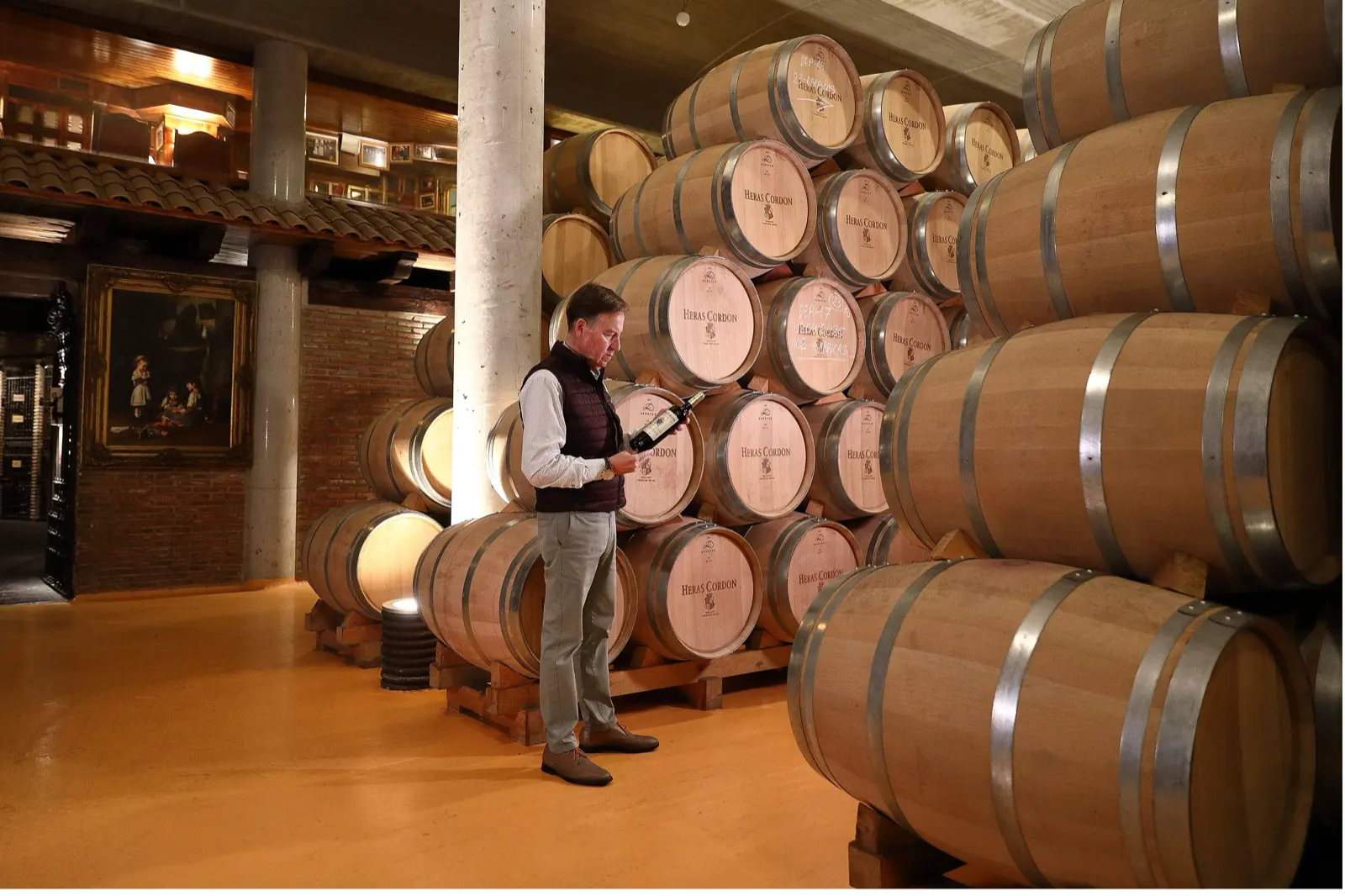 A man reading a bottle label among stacked Heras Cordón barrels