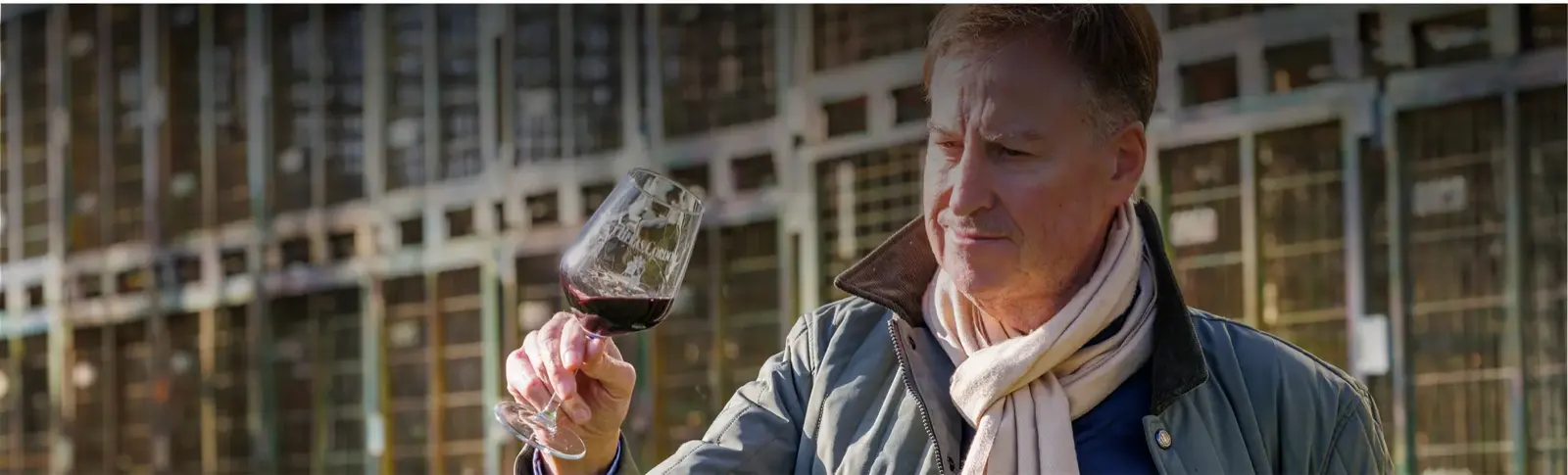 A man in a scarf studying a glass of red wine in the cellar