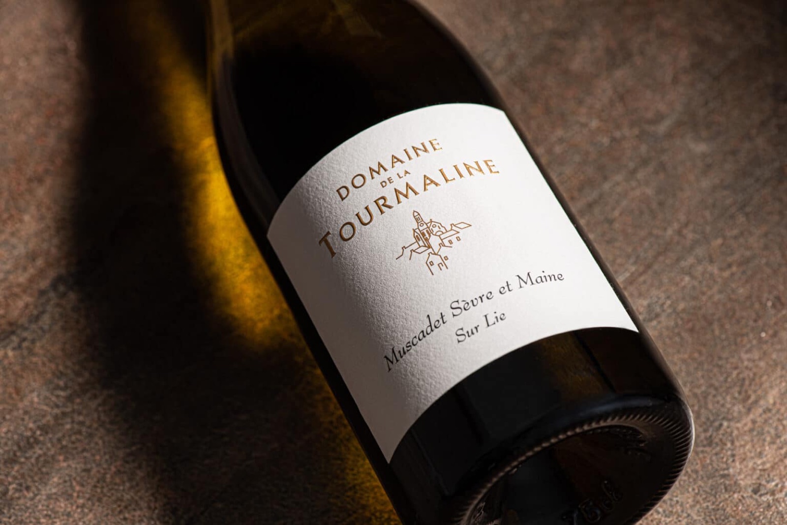 A bottle of Domaine de la Tourmaline Muscadet lying on a stone surface